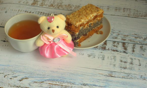 Sponge cake with poppy seeds on a plate, a cup of tea and a teddy bear lying on a wooden table. Close-up.