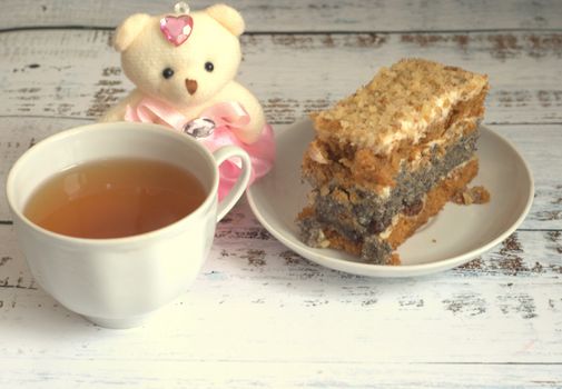 Sponge cake with poppy seeds on a plate, a cup of tea and a teddy bear lying on a wooden table. Close-up.