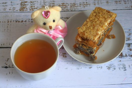 Sponge cake with poppy seeds on a plate, a cup of tea and a teddy bear lying on a wooden table. Close-up.