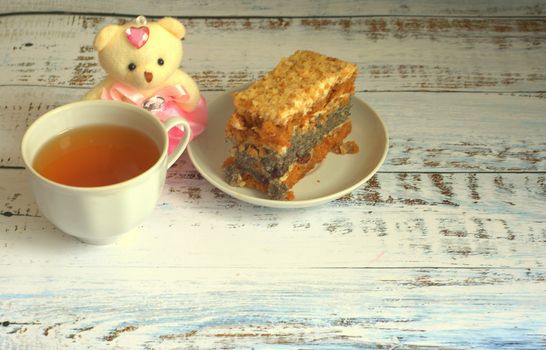 Sponge cake with poppy seeds on a plate, a cup of tea and a teddy bear lying on a wooden table. Close-up.