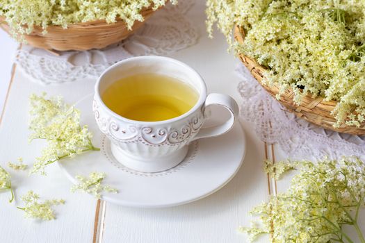 A cup of herbal tea with fresh elder flowers on a white background