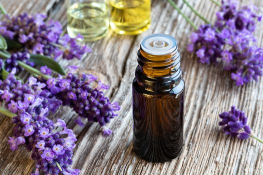 A bottle of essential oil with fresh blooming lavender twigs on a wooden background