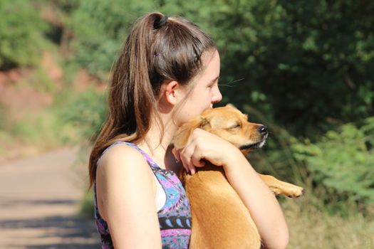 Pretty eighteen year old girl lovingly holding her little dog outside in the warm sunshine as they take a break during a long walk