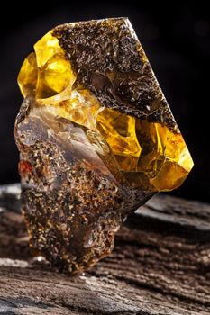 A piece of dirty amber with transparent yellow layer, has superficial cracks on its surface and many inclusions. Polished. Placed on piece of stoned wood.