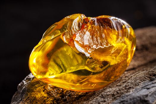 A piece of yellow clean transparent natural amber, classification color Clear Succinite, has some imprints on its surface. Polished, has partly natural shape. Placed on dark stoned wood texture.