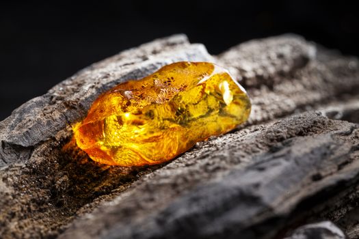 A piece of yellow clean transparent natural amber, classification color Clear Succinite, has some imprints on its surface. Polished, has partly natural shape. Placed on dark stoned wood texture.