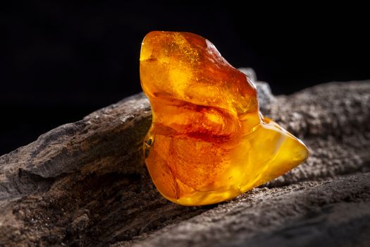 A piece of yellow semi transparent natural amber, classification color honey or cognac, has cracks on its surface. Polished, natural shape. Placed on dark stoned wood texture.