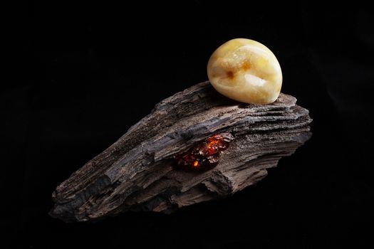 A piece of yellow semi opaque natural amber, classification color Bastard, has cracks inside. Polished, has a bead shape. Placed on dark stoned wood texture.