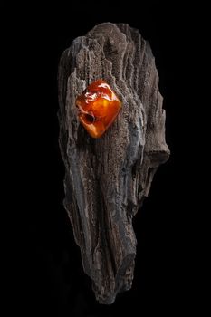 A piece of yellow semi transparent natural amber, classification color honey or cognac, has cracks on its surface. Polished, natural shape. Placed on dark stoned wood texture.