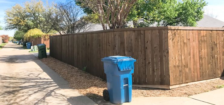 Panorama view empty back alley in residential neighborhood with wooden fence with vines and trash, recycle bin. Quiet suburban area near Dallas, Texas, USA