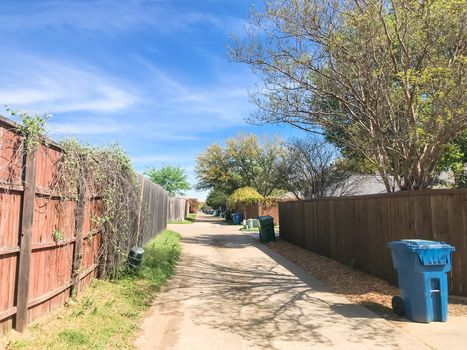 Empty back alley in residential neighborhood with wooden fence with vines and trash, recycle bin. Quiet suburban area near Dallas, Texas, USA