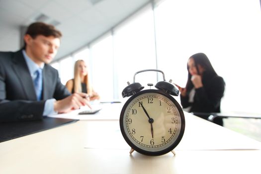 Alarm clock on office table with business discussion people group or meeting team background
