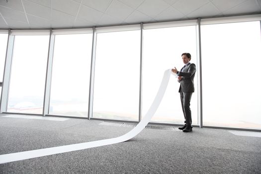 Businessman or male lawyer unrolling and reading long paper list in office