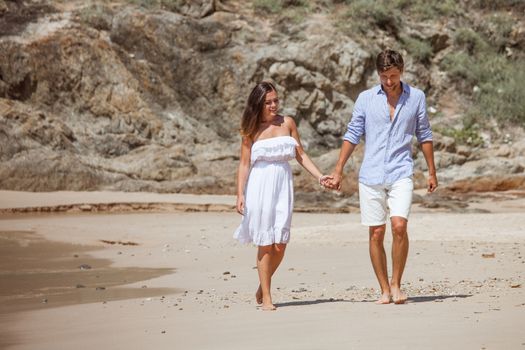 Happy couple walking on sand of tropical beach