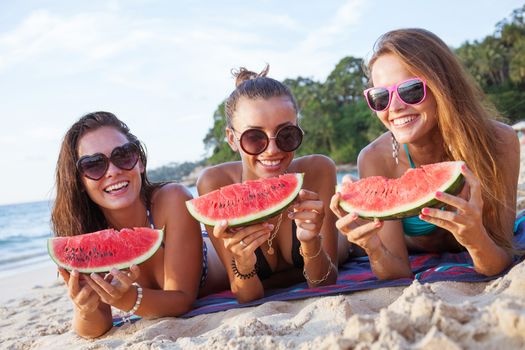 Happy smiling female friends eating watermelon on beach