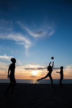 Group of young people playing volleyball on beach at sunset