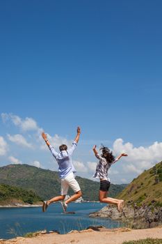 Young couple jumping, beautiful sea view on background