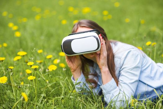 Woman using the virtual reality headset outdoors laying in spring flower field