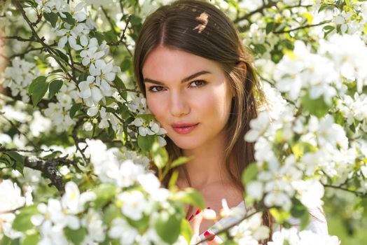 Beautiful young brunette woman standing near blooming apple tree