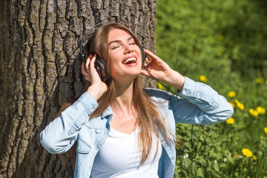 Young brunette woman with headphones listening to the music in park on sunny summer day
