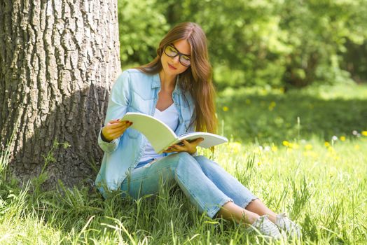 A young brunette woman outdoors in park with a magazine