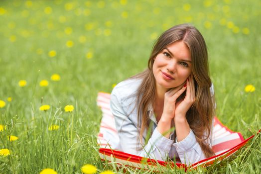 Beautiful young woman laying on grass with dandelion flowers in park