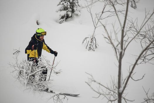 Happy smiling skier walks in the mountains in deep snow after freeride alpine skiing with ski on shoulder