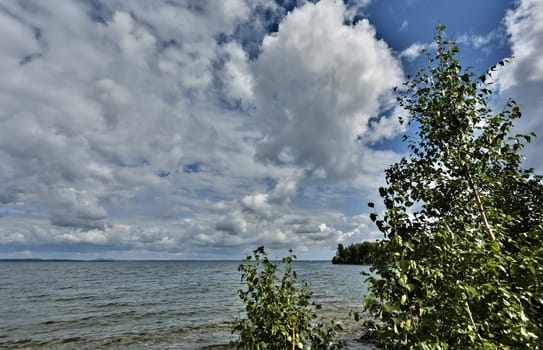 wooded shore against the lake and cloudy sky on a Sunny summer day