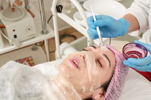 Young woman in beauty salon doing peeling and facial cleansing procedure. Cosmetic multifunctional device. Ultrasound procedure. Medical equipment healthcare. Face professional massage.