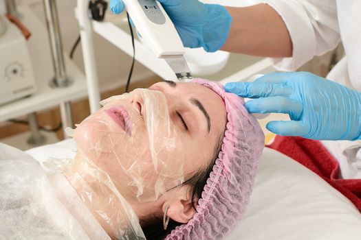 Young woman in beauty salon doing peeling and facial cleansing procedure. Cosmetic multifunctional device. Ultrasound procedure. Medical equipment healthcare. Face professional massage.