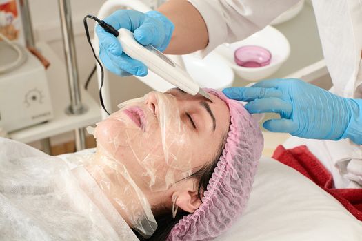 Young woman in beauty salon doing peeling and facial cleansing procedure. Cosmetic multifunctional device. Ultrasound procedure. Medical equipment healthcare. Face professional massage.