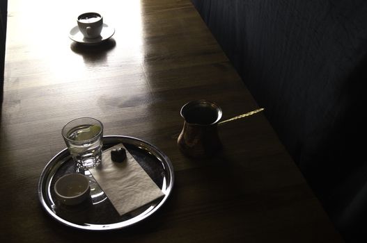 a glass of coffee with coffee pot and chocolate beside a coffee with milk in a white cup placed on a brown table