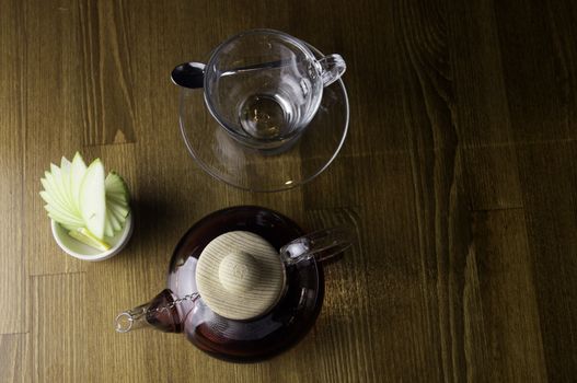 a glass of brewed tea and a glass with lemon in a glass teapot placed on a brown table