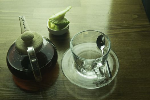 a glass of brewed tea and a glass with lemon in a glass teapot placed on a brown table