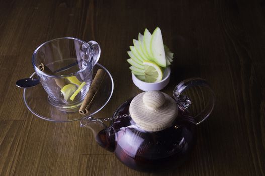 a glass of brewed tea and a glass with lemon in a glass teapot placed on a brown table