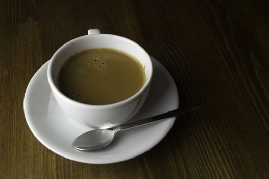 a cup of coffee and spoon placed on a brown table