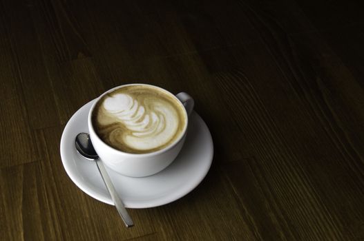 coffee with milk in a white cup on a brown table and spoon to mix