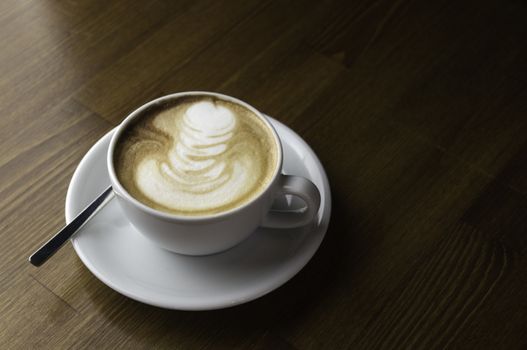 coffee with milk in a white cup on a brown table and spoon to mix