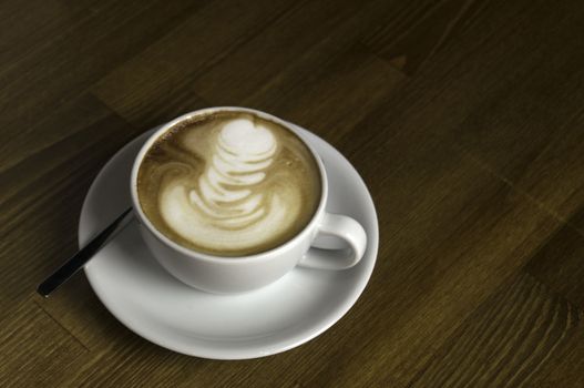 coffee with milk in a white cup on a brown table and spoon to mix