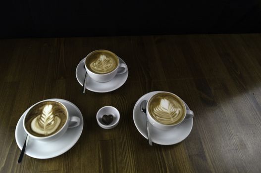three milk coffee in a white cup on a brown table and chocolate next to it