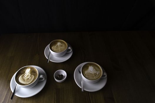 three milk coffee in a white cup on a brown table and chocolate next to it