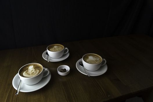 three milk coffee in a white cup on a brown table and chocolate next to it