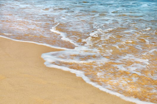 Summer holiday background. Small wave and foam, yellow, clean sandy beach.