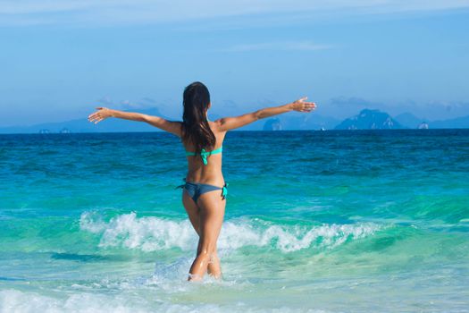 Beautiful happy girl walking to tropical sea with arms raised