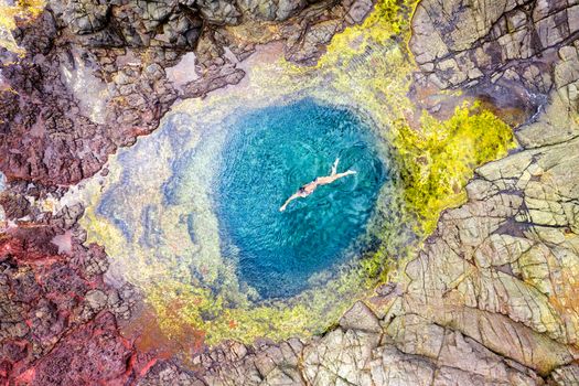 Aerial shot of a woman swimming in a crystal clear blue water swimming hole rock pool