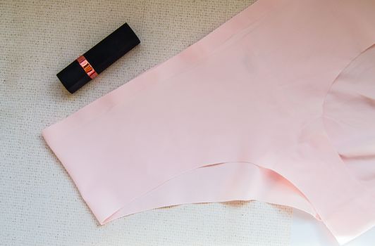 Flat lay women's accessories - underwear and cosmetics.The view from the top women's pink bikini panties and lipstick. The concept of buying women's things, women's day.