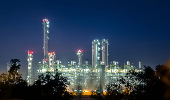 view of petrochemical and petroleum plant industry with refinery stack and tank farm in in chemical industrial zone at night after sunset