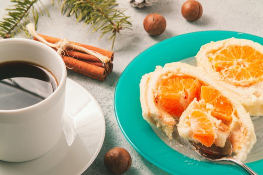 Sweet roll with whipped cream and tangerine filling and Christmas decorations and a cup of coffee.