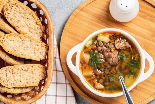 Lentil soup with chicken in a white bowl on a wooden board, top view.