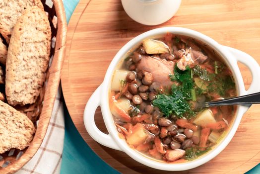 Lentil soup with chicken in a white bowl on a wooden board on a blue table, top view.